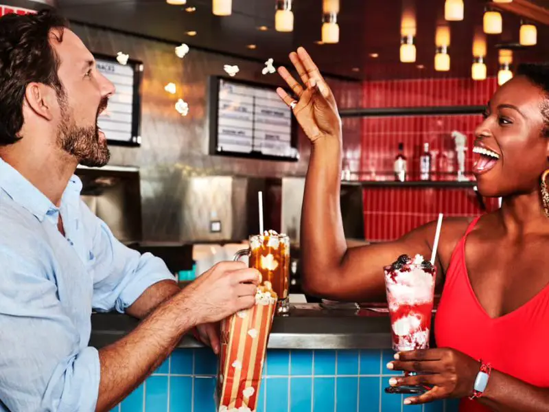 Two people drinking milkshakes and eating popcorn at a diner-style bar