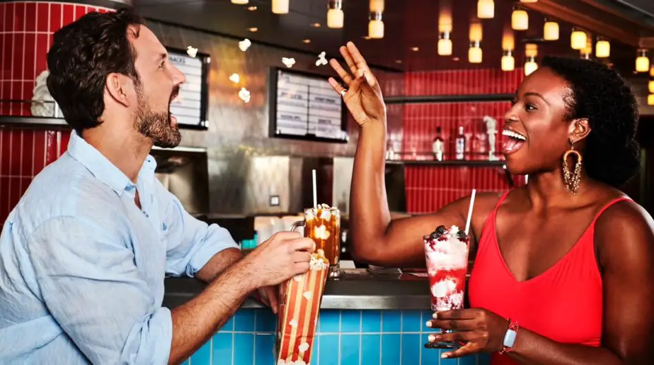 Two people drinking milkshakes and eating popcorn at a diner-style bar