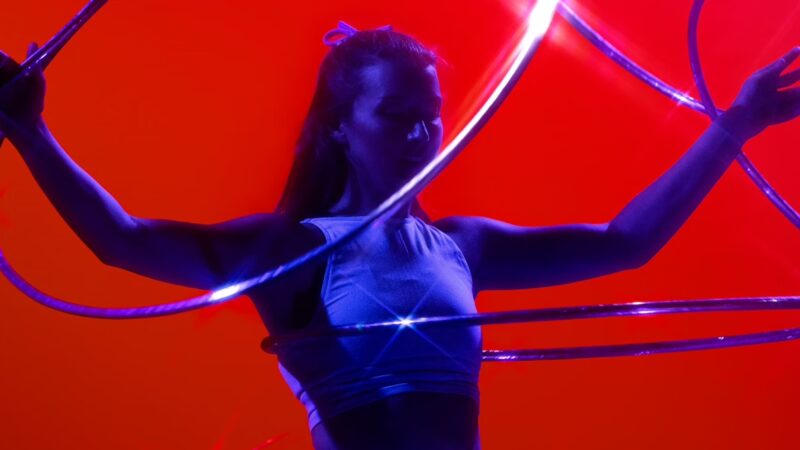 A woman spinning 5 hula hoops lit in blue, with a red backdrop