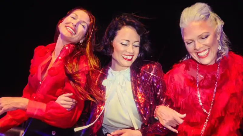 A group of three laughing people holding each other with sparking red clothing