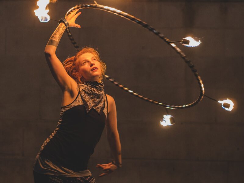 A circus performance where a person is swinging a hula hoop above their head that has flaming points attached to it