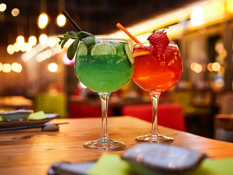 Two colourful cocktail drinks against a brightly lit bar background