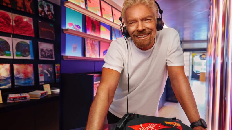 Sir Richard Branson listening to records, with a background of vinyl records