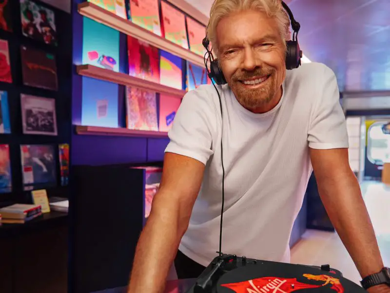 Sir Richard Branson listening to records, with a background of vinyl records