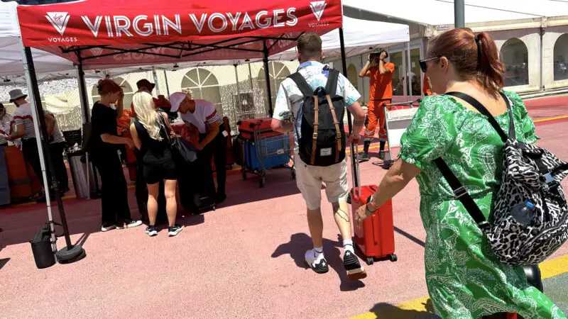 Cruise passengers making their way to a luggage drop-off point labelled 'Virgin Voyages' in red