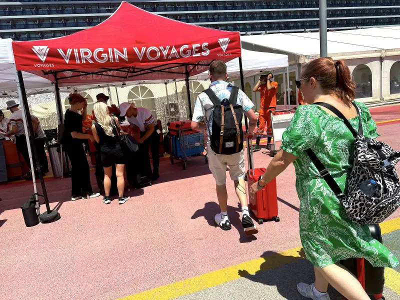 Cruise passengers making their way to a luggage drop-off point labelled 'Virgin Voyages' in red