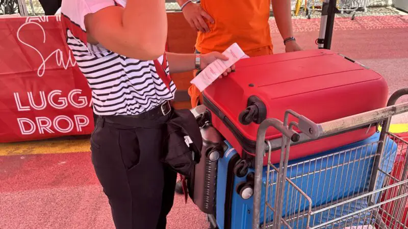 A stack of luggage on a luggage trolley being labelled by a person wearing a striped t-shirt