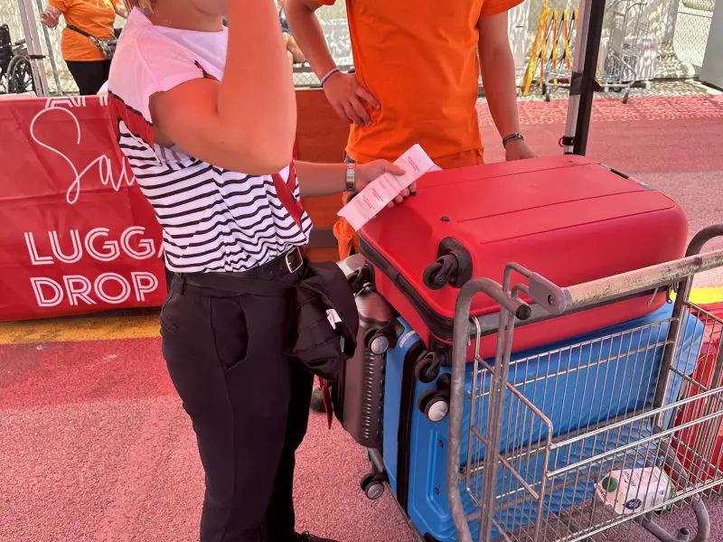A stack of luggage on a luggage trolley being labelled by a person wearing a striped t-shirt
