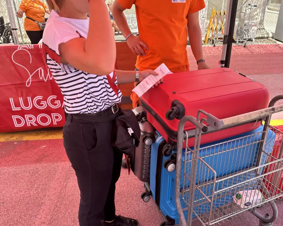 A stack of luggage on a luggage trolley being labelled by a person wearing a striped t-shirt