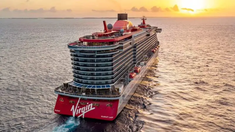 A Virgin Voyages cruise ship sails towards an orange sunset