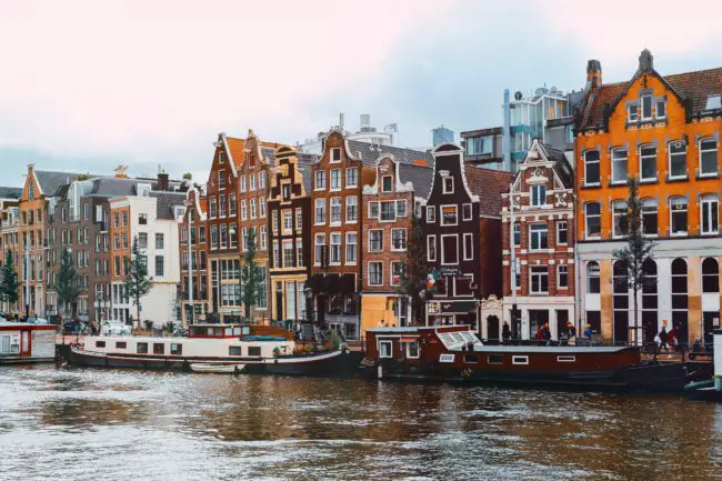 A canal in Amsterdam with banks surrounded by colourful buildings and bicycles