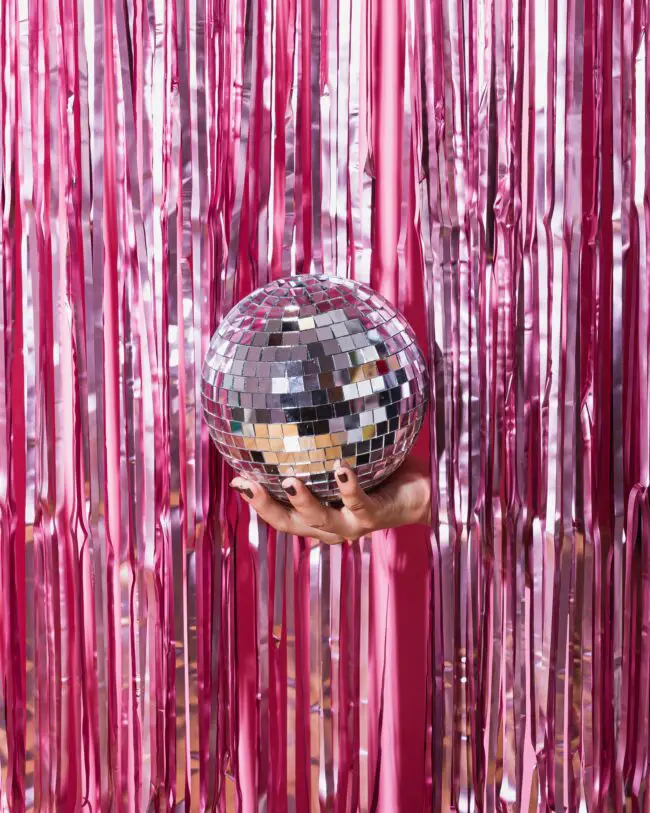 a disco ball being held in front of a pink glittering curtain