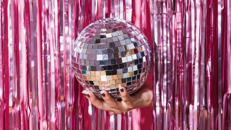 a disco ball being held in front of a pink glittering curtain