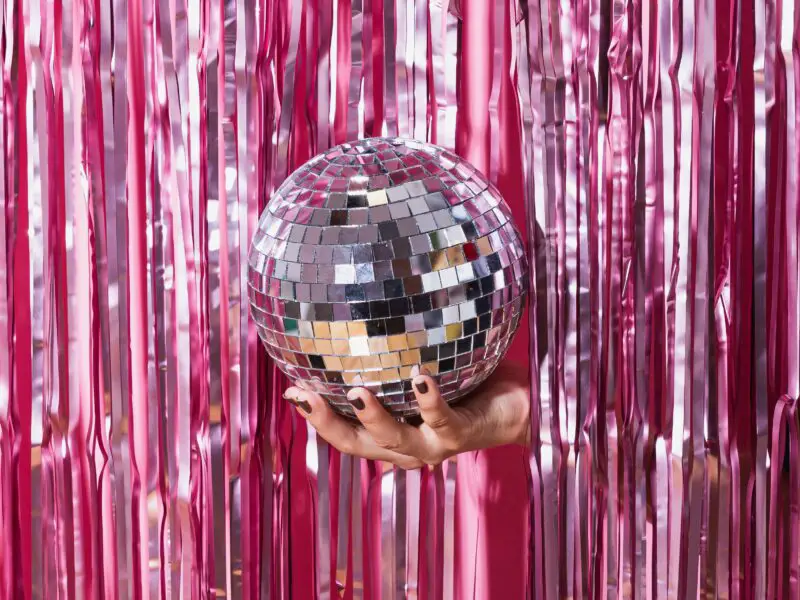 a disco ball being held in front of a pink glittering curtain
