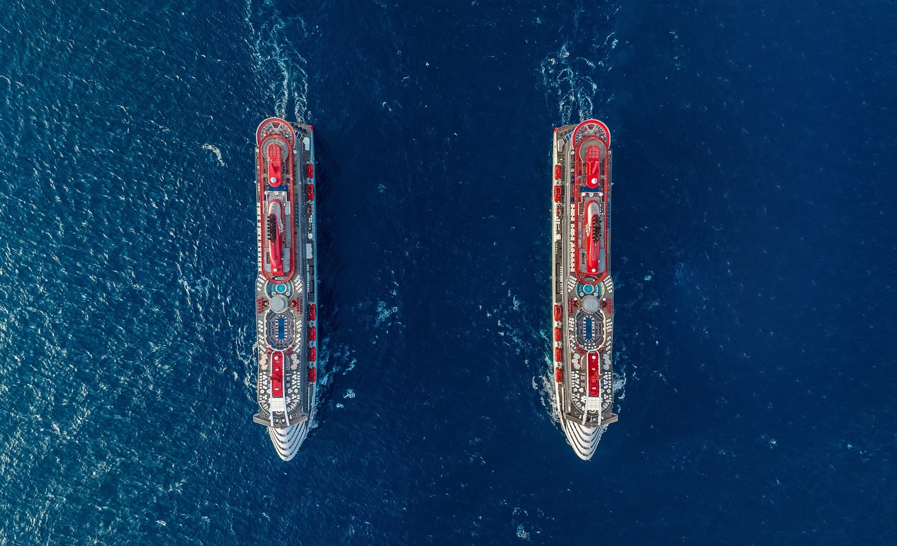 Valiant Lady and Scarlet Lady cruise ships sailing in the ocean side by side
