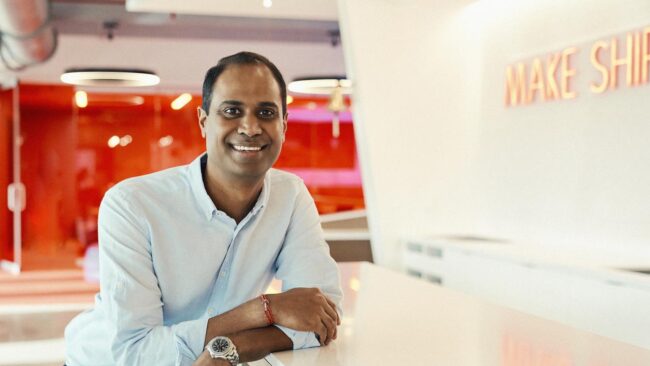 Virgin Voyages CEO Nirmal Saverimuttu sitting against a white and red background