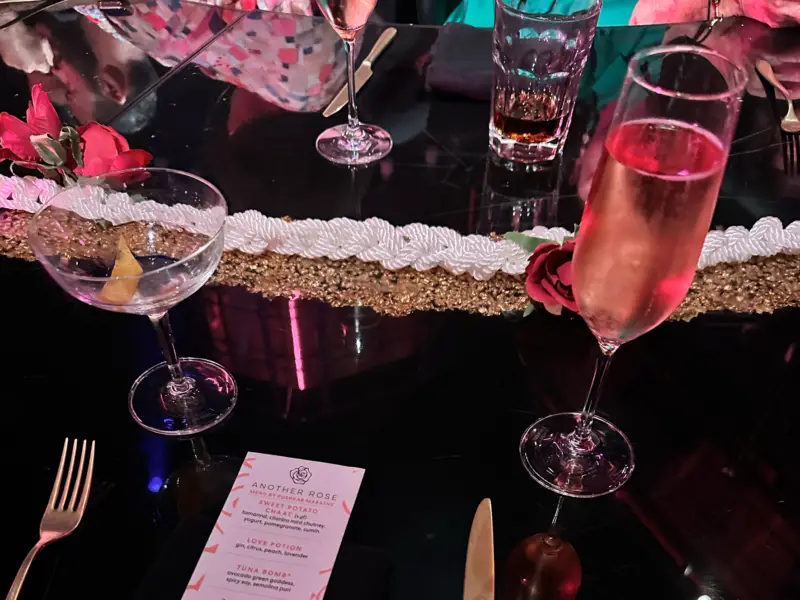 A table filled with drinks, the top of a menu with the words 'Another Rose' is in view