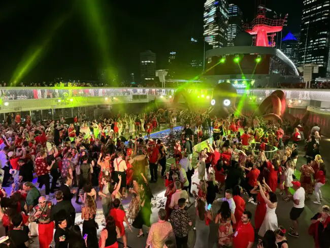 hundreds of people dressed in red dancing around a pool