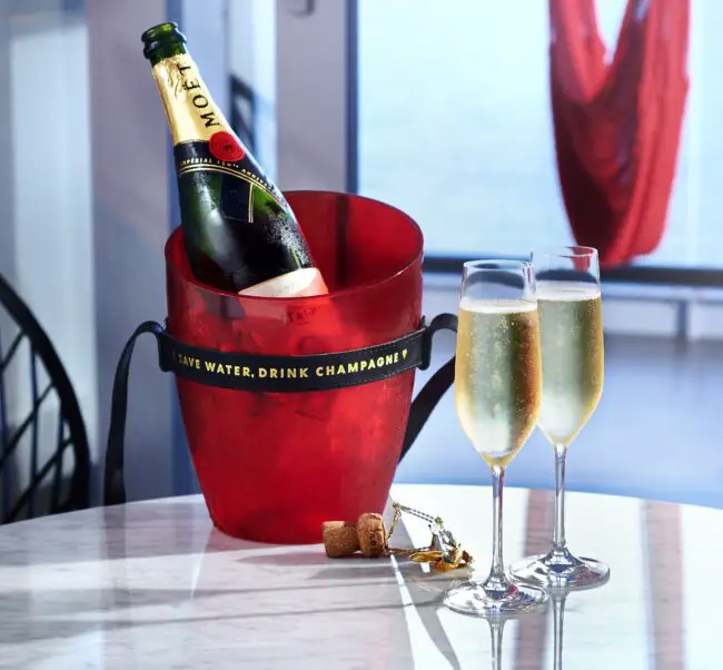 A bottle of Moet champagne in a bucket and two full glasses on a table in a suite, ordered through the Sailor App's Shake for Champagne feature.
