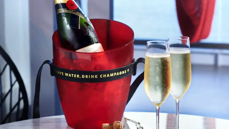 A bottle of Moet champagne in a bucket and two full glasses on a table in a suite, ordered through the Sailor App's Shake for Champagne feature.