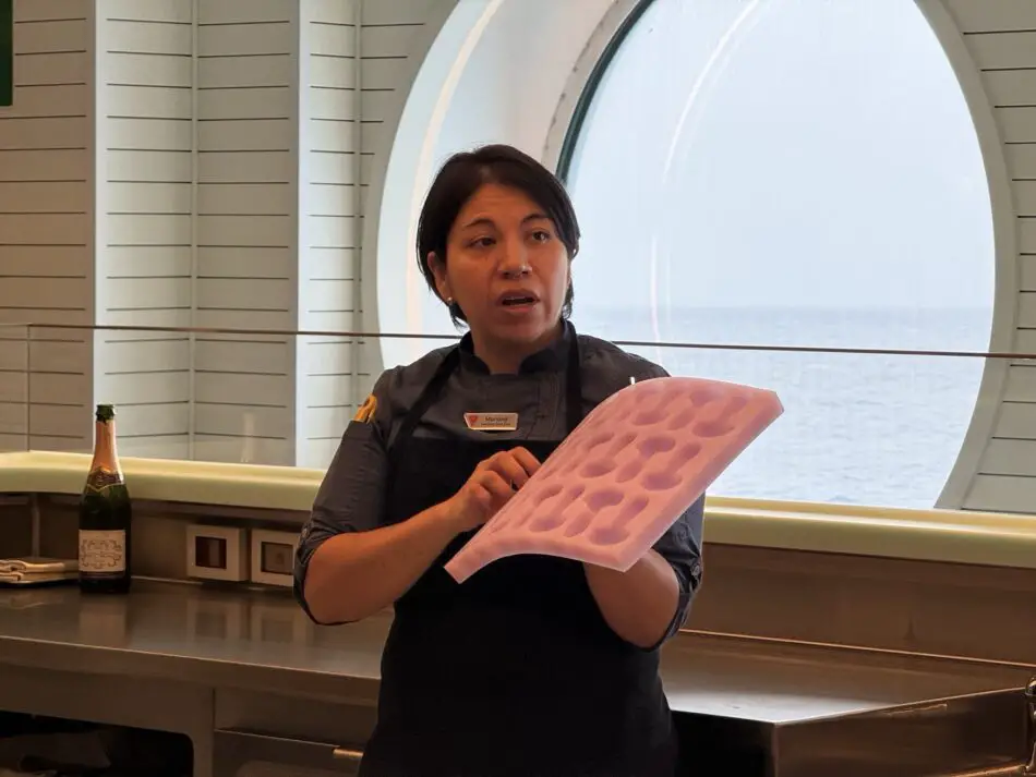 Cruise ship staff member demonstrates pink silicone tray in a galley beside a circular ocean-view window