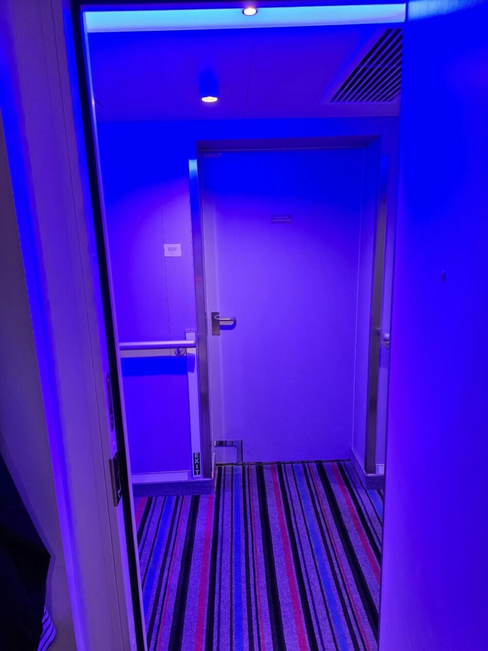 Blue-lit corridor leading to a Virgin Voyages cabin door