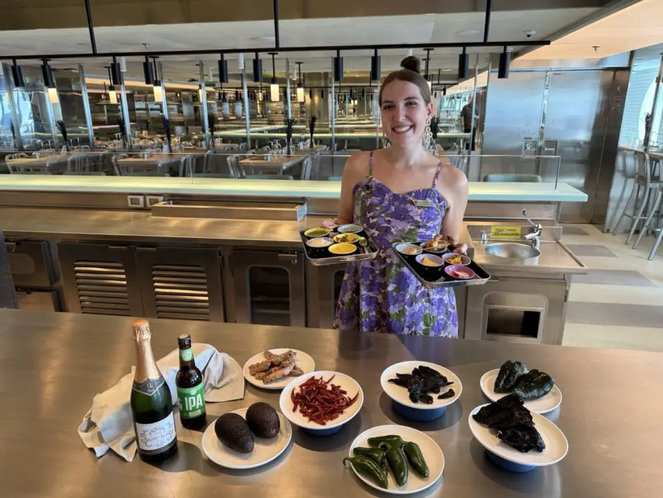 Faith the Foodie stands above a steel table with ingredients including peppers, avocado and ginger with wine and beer