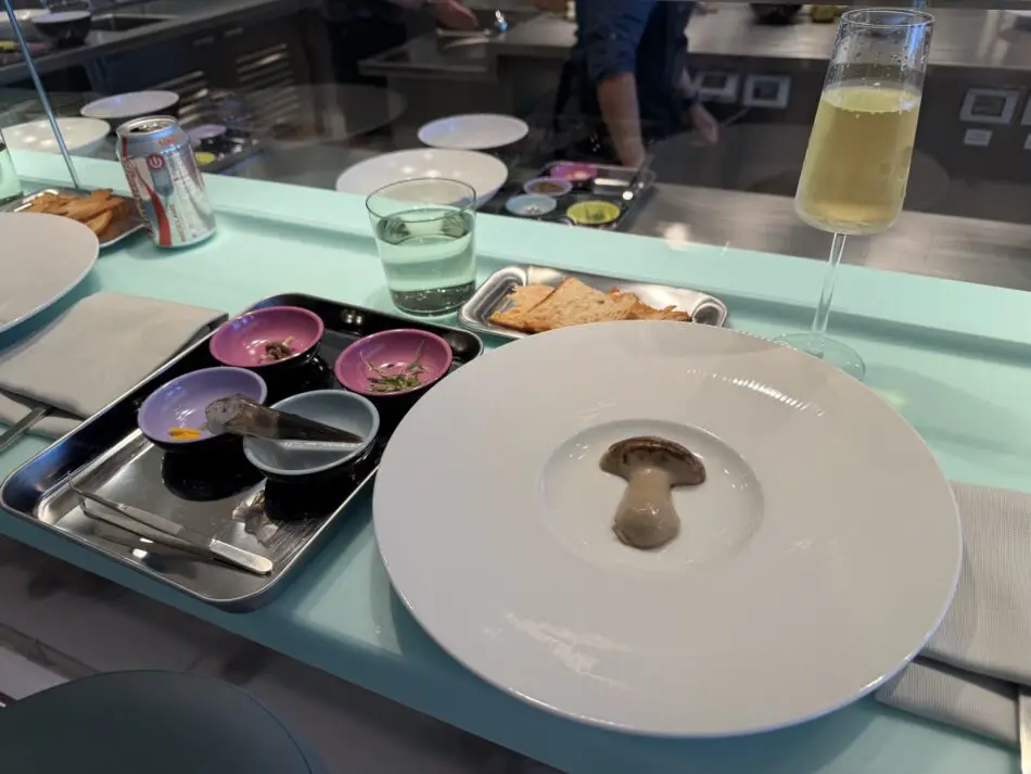 Mushroom dish on a white plate beside a champagne glass in a cruise cabin dining area