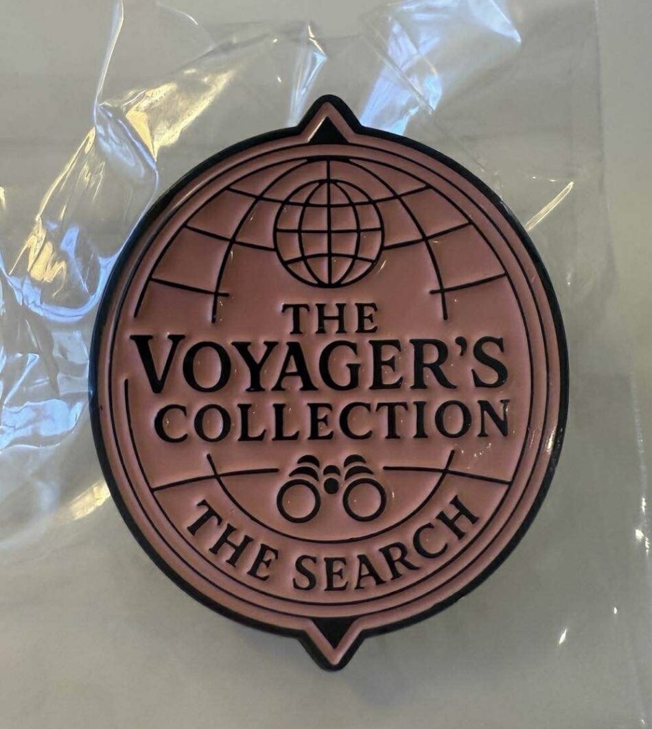 Pink circular pin featuring The Voyager's Collection The Search and globe emblem