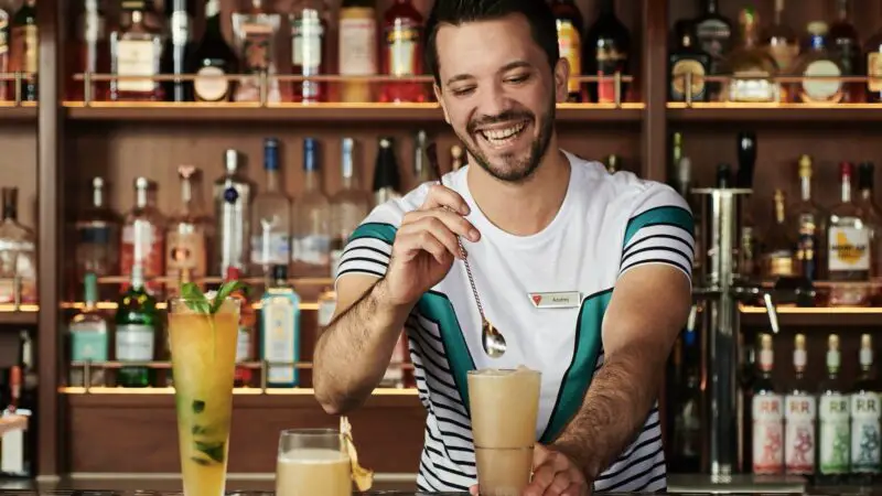Smiling bartender mixes a cocktail behind a well-stocked bar