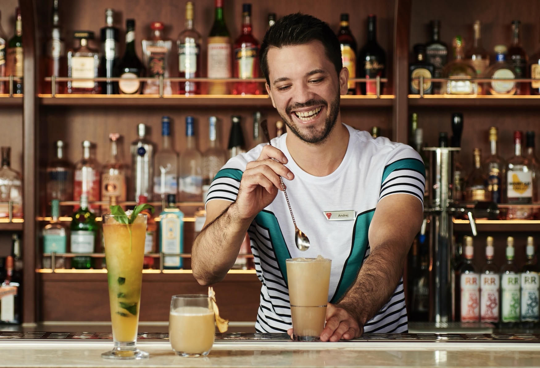 Smiling bartender mixes a cocktail behind a well-stocked bar
