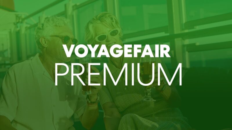 Two seniors in sunglasses toast with drinks inside a Virgin Voyages cabin with VOYAGEFAIR PREMIUM overlay
