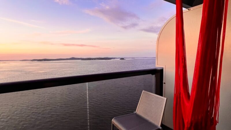 Virgin Voyages cruise ship balcony with white chairs and red hanging hammock overlooking sunset over the sea