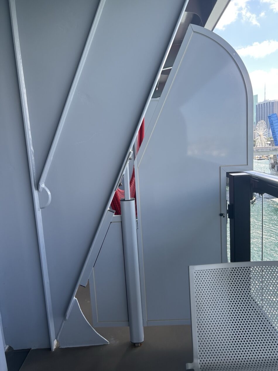 Exterior of a cruise ship cabin with curved metal panels and a glass railing overlooking the water