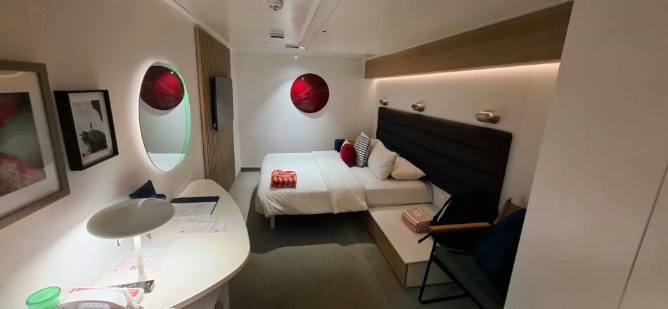 Cruise cabin with a double bed, desk, and seating on a Virgin Voyages cruise ship