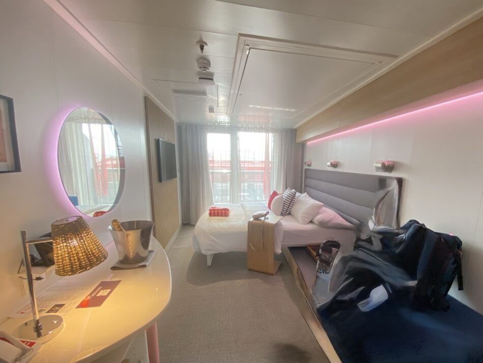 Virgin Voyages cruise ship cabin with bed, desk, and pink lighting