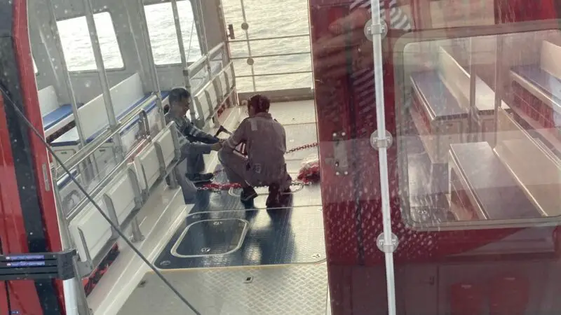 Two people sitting on the deck of a red Virgin Voyages cruise ship with water in the background