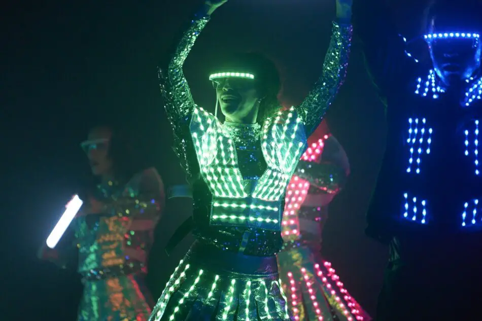 Dancers wearing glowing LED costumes perform on stage