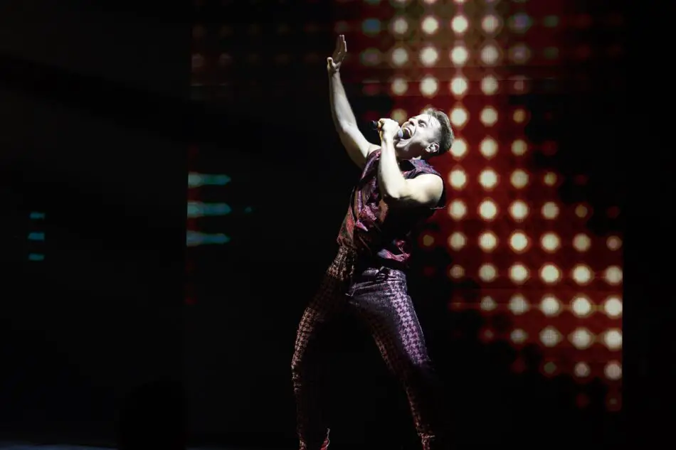 Male singer performing on a concert stage with microphone and red bokeh lights