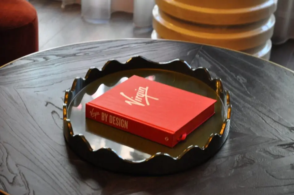 Red Virgin By Design book on a dark round table at Virgin Hotels London Shoreditch