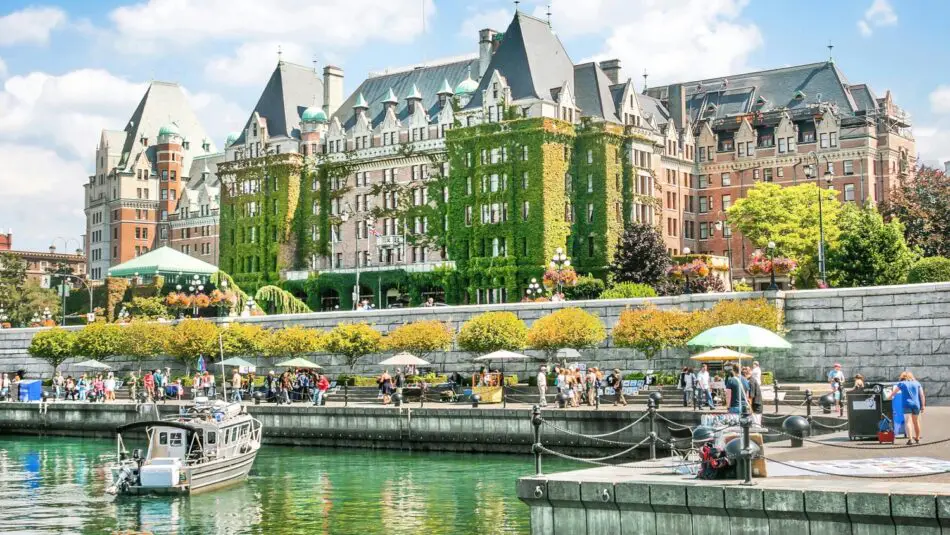 Ivy-covered hotel along a riverfront with people strolling and a moored boat