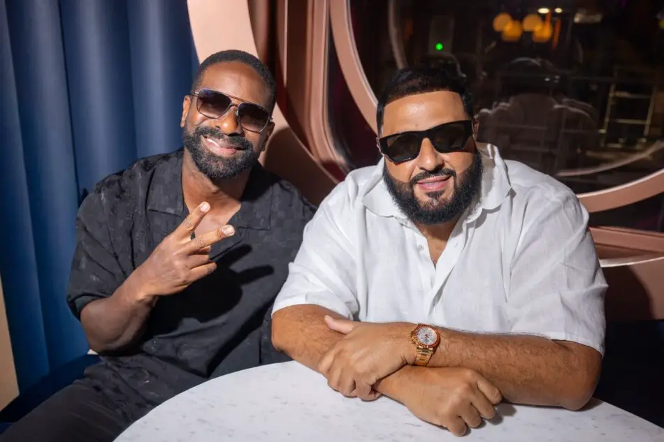 Two men in sunglasses sit at a table in a Virgin Voyages cruise ship cabin