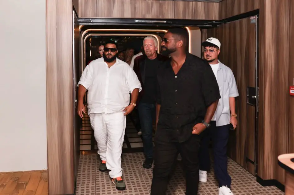 Group of men walking through an open elevator doorway in a wood-paneled corridor