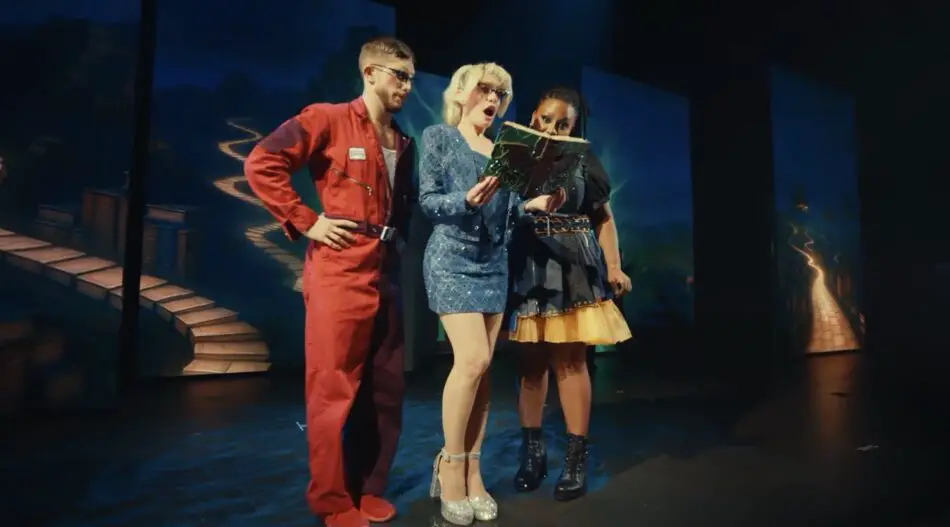 Three performers on a stage reading a large book together