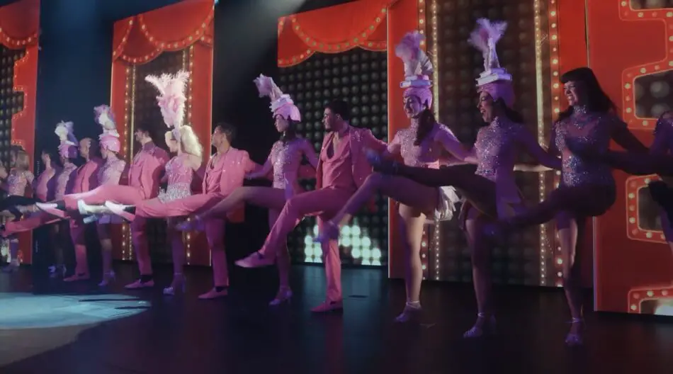 Stage performance of dancers in pink sequined costumes with feathered headdresses