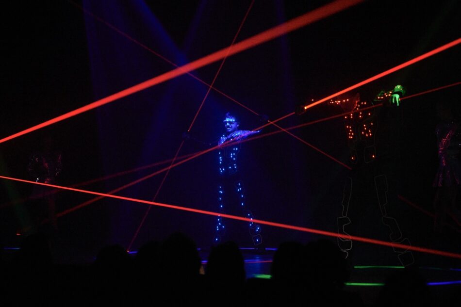 Performer in blue LED suit on laser-lit stage