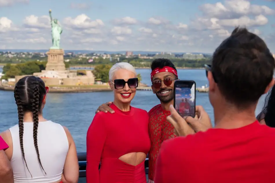 People posing for a selfie on a Virgin Voyages ship with the Statue of Liberty in the background