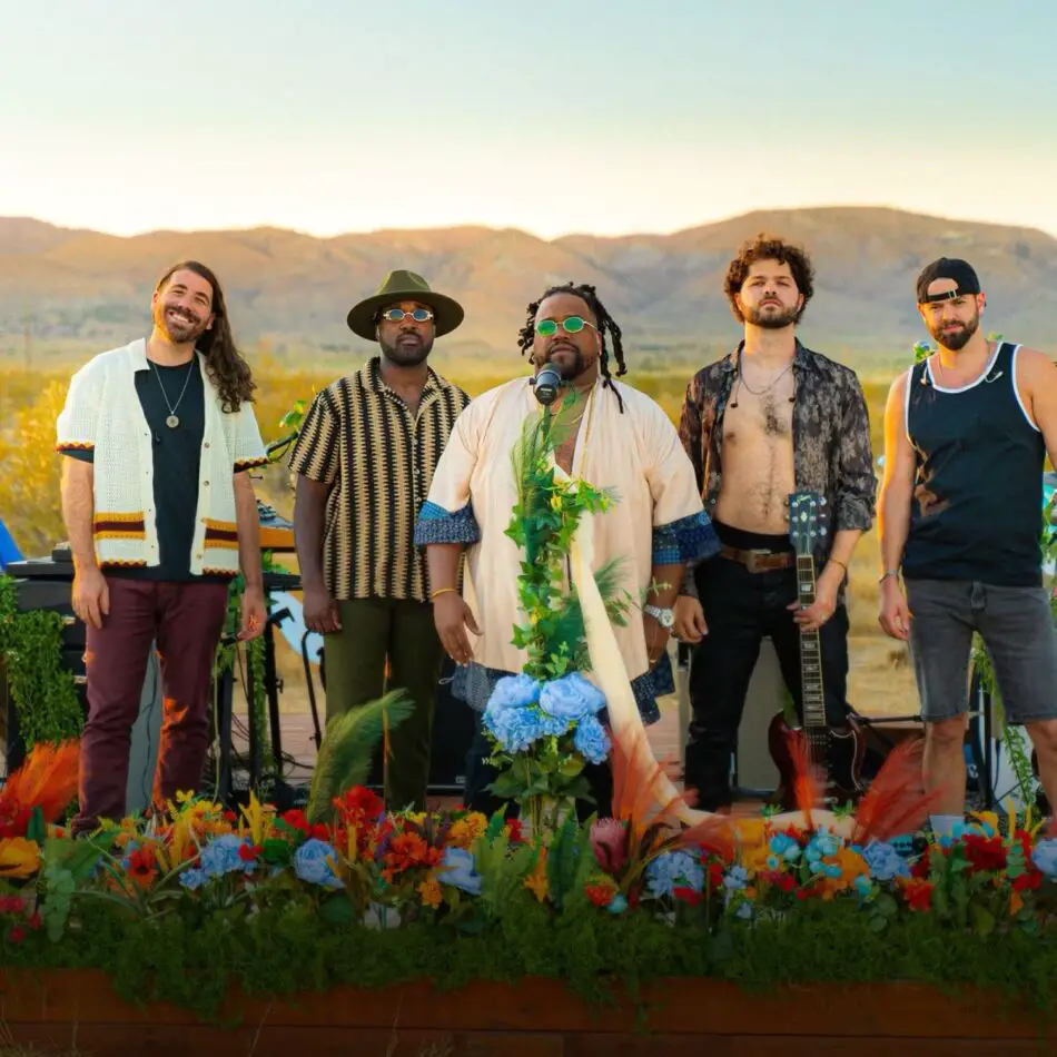Five musicians pose on an outdoor stage in a desert setting