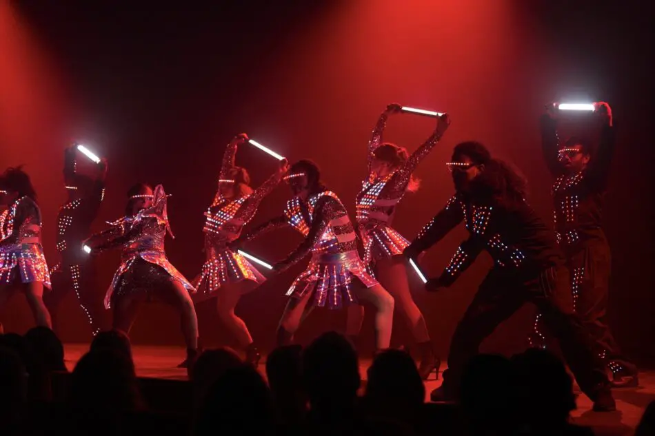 Dancers in LED outfits perform on a stage with red lighting