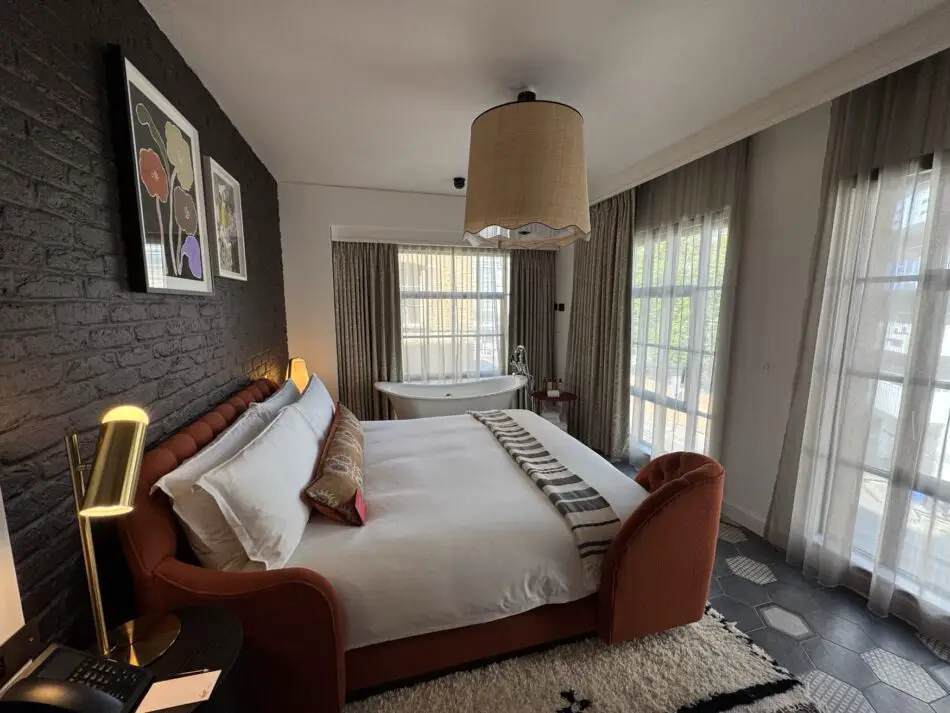 Luxurious hotel suite bedroom with brick accent wall, bed, and freestanding bathtub in a Virgin Hotel in London